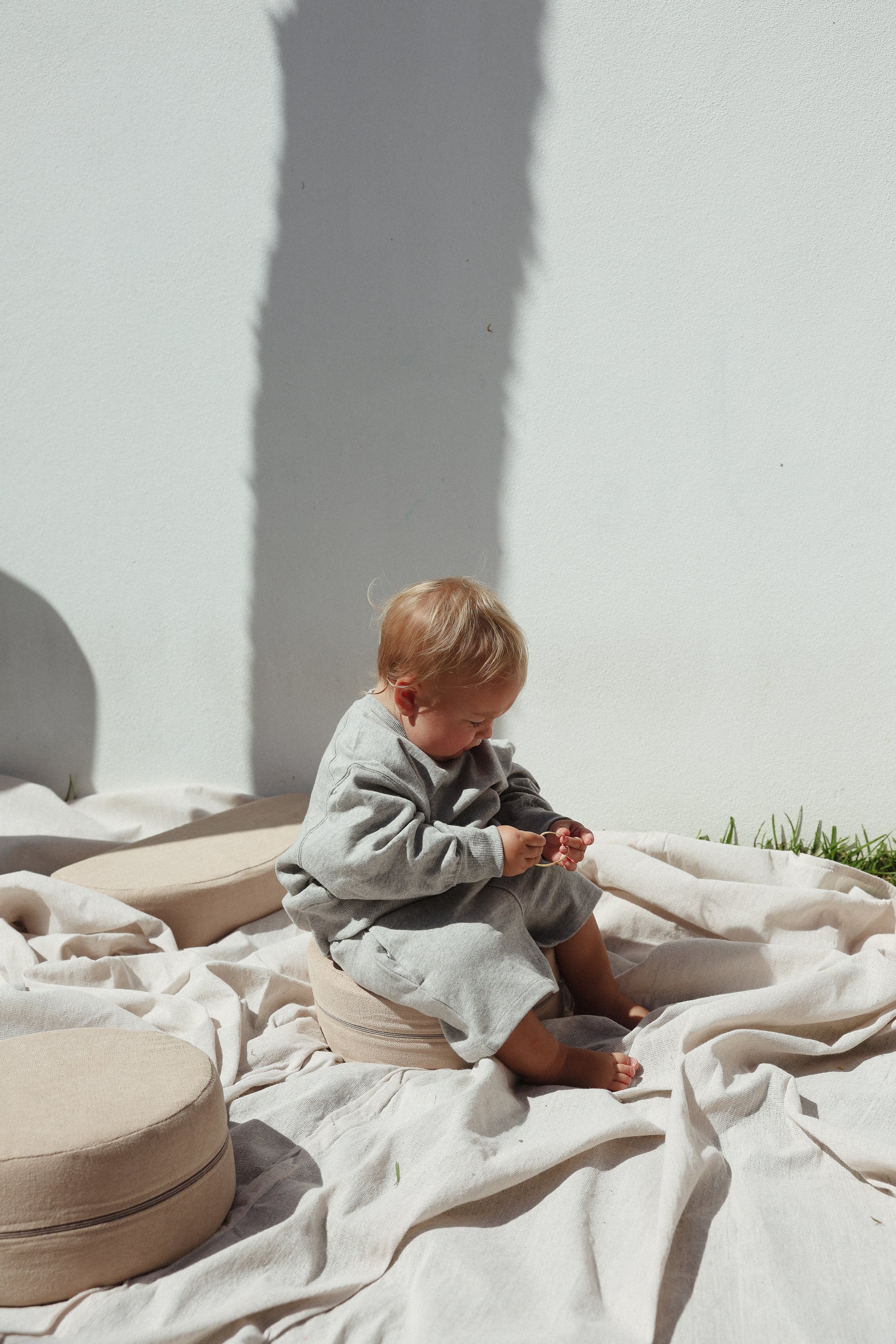Child sitting on a blanket against a white wall with soft shadows