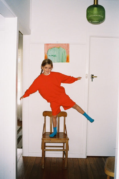 Person in a red dress standing on a wooden chair in a room with a white door and green lamp.