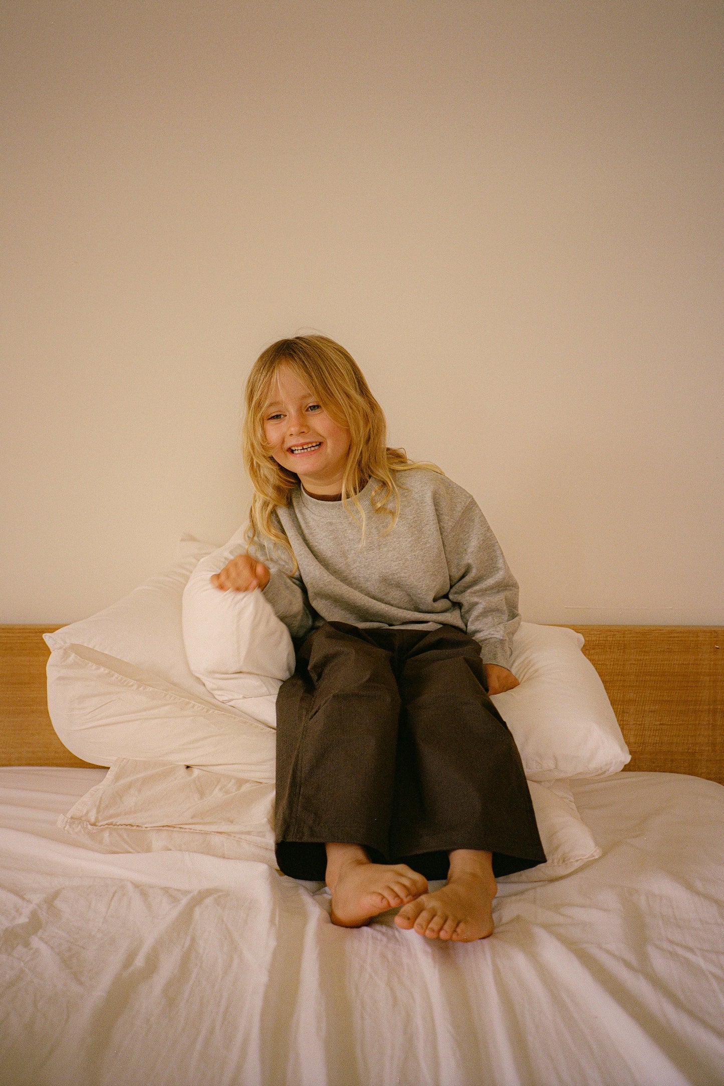 Child sitting on a bed with white pillows and a wooden headboard.